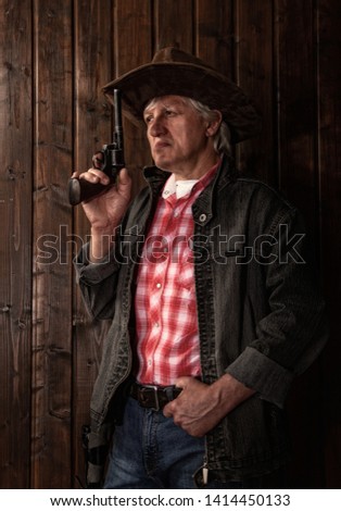 classically dressed middle aged cowboy stands with a revolver in a dark room with wooden walls