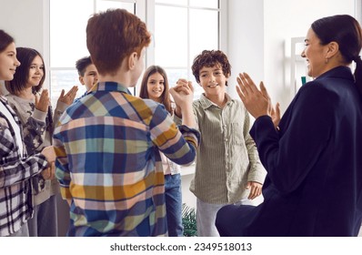 Classmates meeting after summer holidays. Happy smiling school children shaking hands greetings each other in the classroom with their friendly woman teacher. Back to school and education concept. - Powered by Shutterstock