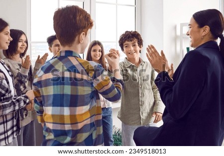Classmates meeting after summer holidays. Happy smiling school children shaking hands greetings each other in the classroom with their friendly woman teacher. Back to school and education concept.