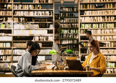 Classmates in a study group taking notes on laptop or notebook, studying coursework at wooden table library.