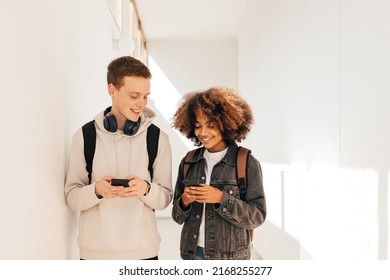 Classmates walking in corridor. Boy and girl in school and looking on their smartphones.