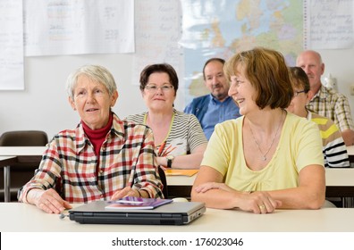 A Classroom With Older Persons Sitting At Desks.