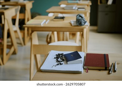 Classroom setting with desks and study materials including books, notebooks, and Roman Catholic rosary placed on table. Environment exuding calmness and academic focus