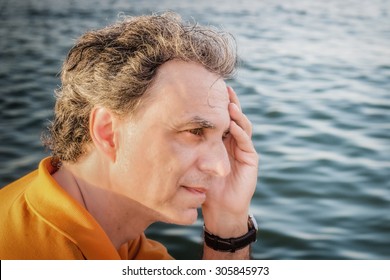 Classy  40 Years Old Sportsman With Three-day Beard And Salt And Pepper Hair Wearing An Orange Polo Shirt While He Is Thinking In Front Of The Sea