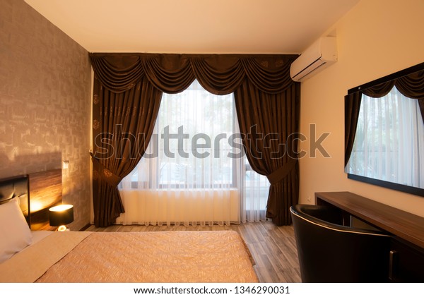 Classy bedroom interior design. Large bed.\
Room with brown color tone furniture. Windows with long curtains,\
drapery and sheers. Interior\
photography