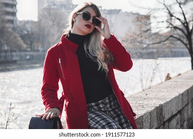 Classy blond lady in red coat. Urban photoshoot on sunny winters day.