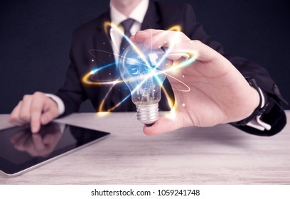 A classy businessman holding a colorful light bulb with shining circles in front of dark background concept. - Shutterstock ID 1059241748