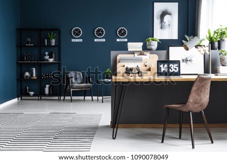 Classy, dark blue home office interior for a global businessman with elegant furniture and a computer on a wooden desk
