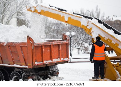 Claw Loader Vehicle Removes Snow From The Road.  Uniformed Community Service Worker Helps Load Snow Into A Truck.