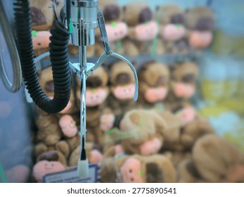 Claw Machine Close Up Focus on Metal Claw with Blurred Stuffed Toy Prizes Background. Close-up view of Mechanical Claw Machine Game.
