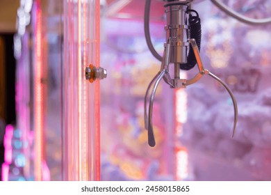 A claw machine with a red light on it. The claw is grabbing dolls. The machine is in a neon pink room