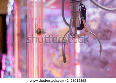 A claw machine with a red light on it. The claw is grabbing dolls. The machine is in a neon pink room