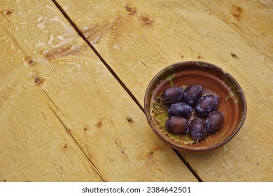 Clay bowl with a bunch of plums standing on the wooden table. Above view.  - Powered by Shutterstock