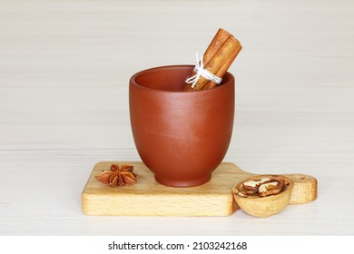 A clay brown glass with a bunch of cinnamon on a small cutting board. On the left there is a star anise, on the right there is a half of a walnut. Light background, close up. Still life, rustic styl - Shutterstock ID 2103242168