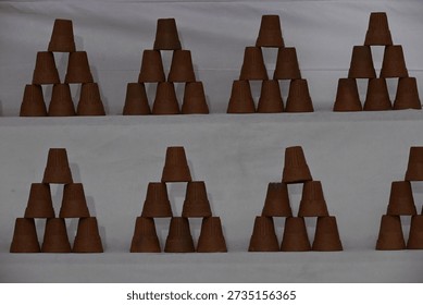 Clay cups are stacked in a triangular formation on white shelves.