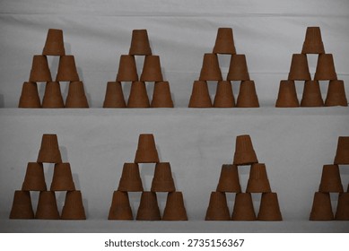 Clay cups are stacked in a triangular formation on white shelves.