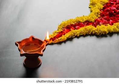 Clay diya lamp with decorative marigold and rose flower petals rangoli on the floor for Diwali festival.