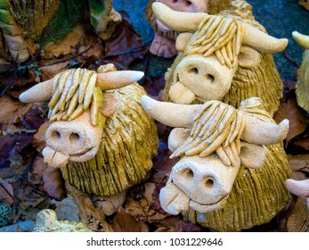 Clay figures of long horned hairy Highland Cattle in a woodland fantasy garden amid naturally fallen leaves and twigs