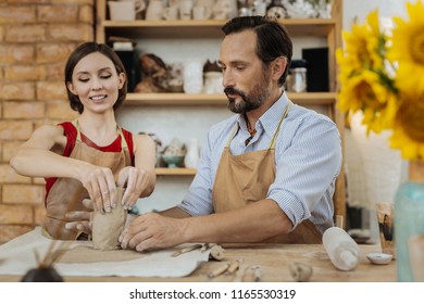 Clay item. Beaming dark-haired woman wearing red shirt and brown apron making clay item