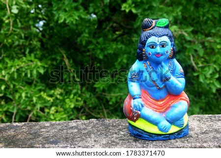 a clay model of Indian god Krishna , with trees in background