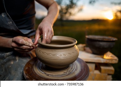 Clay potter creating on the pottery wheel. Sculptor from fresh wet clay on pottery wheel. Selected focus. Hands of young potter was produced on range of pot in open air - Powered by Shutterstock