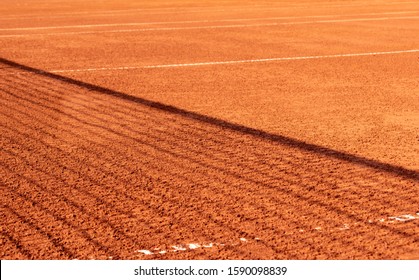 Clay Tennis Court With A Net Shadow On It. Season Of The Game On The Open Red Clay Tennis Court. Orange. Background, Texture, Space For Text.