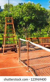 Clay Tennis Court In A Resort Garden Setting With Wooden Bench And Umpire Chair