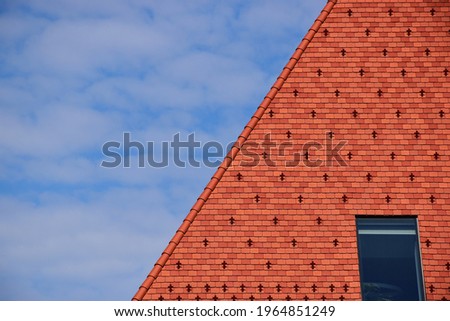 clay tile roof with steep slope in red brown color. roof window or skylight. metal ice and snow guard in square pattern. snow breaker. modern new construction concept. bright blue sky and white clouds