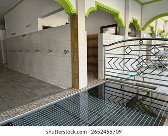 A clean ablution area in a mosque with tiled walls, multiple water taps, and a modern metal gate, used for ritual washing before prayers in Islamic tradition.