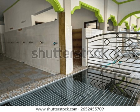 A clean ablution area in a mosque with tiled walls, multiple water taps, and a modern metal gate, used for ritual washing before prayers in Islamic tradition.
