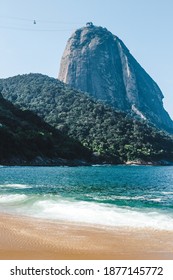 The clean beach and turquoise water of Praia Vermelha in Rio de Janeiro, Brazil, which is backdropped by the travel and tourism landmark Sugarloaf Mountain or Pão de Açúcar