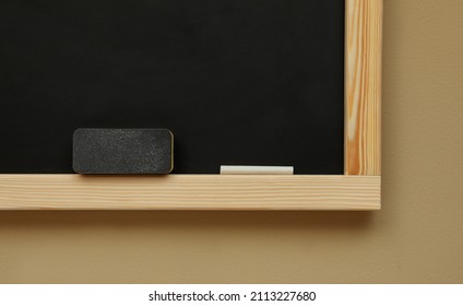 Clean Blackboard With Chalk And Duster Hanging On Beige Wall