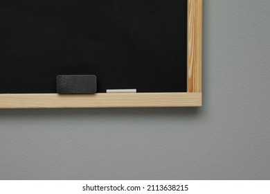 Clean Blackboard With Chalk And Duster Hanging On Grey Wall