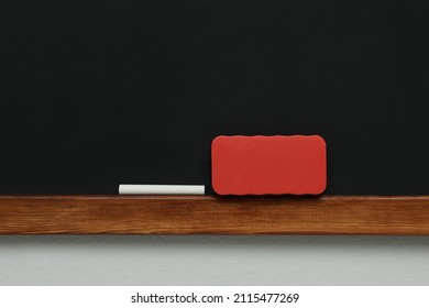 Clean Blackboard With Chalk And Duster Hanging On Grey Wall