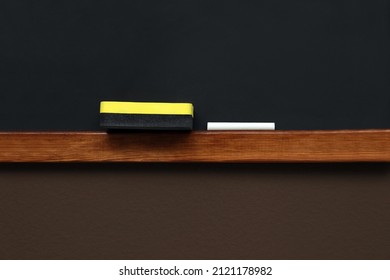 Clean Blackboard With Chalk And Duster Hanging On Brown Wall