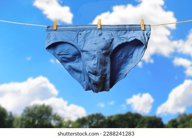 Clean blue men's briefs hanging on rope to dry outdoors on sunny summer day. Clothesline with washed underwear. Regular laundry. Hygiene and clothes care concept