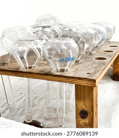 A clean and bright high-angle shot featuring several 250ml glass volumetric flasks inverted on a wooden laboratory drying rack. The high-key lighting creates a sterile and modern atmosphere, emphasizing the clear glass texture and blue measurement markings. Perfect for chemistry, pharmaceutical, clinical research, and education-themed projects.
