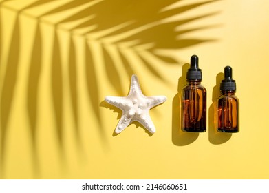 Clean brown glass cosmetic bottles with pipette, starfish, sun shade from tropical leaf on yellow background. Summer concept of natural cosmetics. Spa products for health, beauty. Serum, facial oil