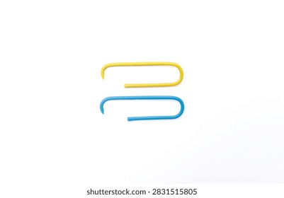 Clean composition showing two large paperclips, one blue and one yellow, attached to the edge of a white sheet.
