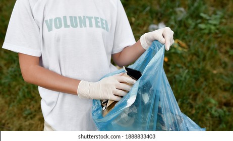 Clean Up Day. Cropped Shot Of A Young Woman Volunteer Wearing Uniform And Rubber Gloves With Trash Bag In Hands Cleaning Forest Or Park From Garbage. Ecology Problems And Nature Pollution