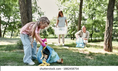 Clean Up Day With Family. Cute Little Girl Holding Trash Bag And Collecting Garbage While Cleaning With Parents In The Park Or Forest. Environmental Conservation And Ecology, Recycling And Concept