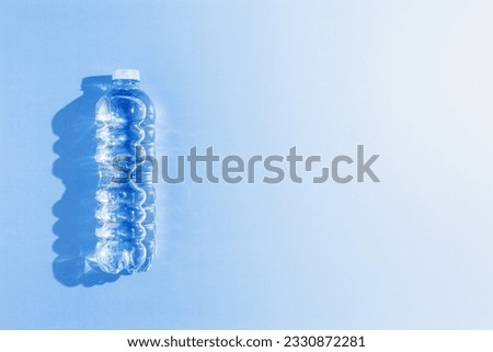 Clean drinking water in small plastic bottle at sunlight, hard shadow on blue background, copy space. Full closed bottle water half litre. Pollution, plastic garbage, non-biodegradable packaging waste