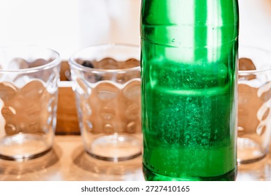 Clean, empty glasses lined up on a table with a green glass bottle in the foreground