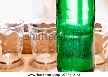 Clean, empty glasses lined up on a table with a green glass bottle in the foreground
