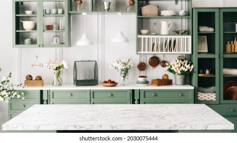 Saubere und leere Marmortheke, grüne Vintage-Küchenmöbel mit vielen Blumen und Schüssel mit Erdbeeren, paarweise aufgehängte Leuchten, verschiedene Geschirr auf unscharfem Hintergrund