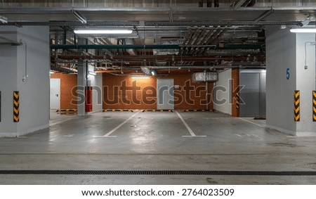 Clean and empty modern underground parking garage with bright lighting, exposed industrial pipes and ducts on ceiling, robust concrete pillars, brick accent walls, and clearly marked parking spaces fo
