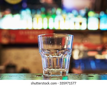 Clean Empty Old Fashion Rocks Tumbler Whiskey Glass On A Dark Bar Counter With A Background Of Neon Lights And Bokeh