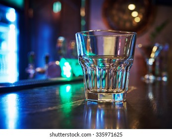 Clean Empty Old Fashion Rocks Tumbler Whiskey Glass On A Dark Bar Counter With A Background Of Neon Lights And Bokeh