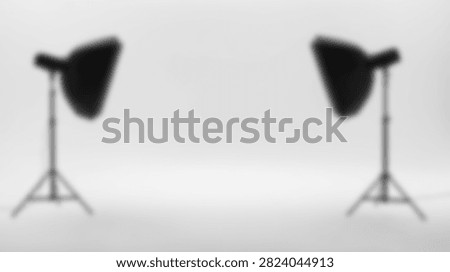 A clean and empty photography studio set up with two professional lighting stands and softboxes against a white backdrop.