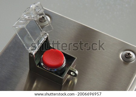 Clean, empty and a round red button with a raised a safety cap. The button is located on a metal box and is ready to use. There are no inscriptions. Close-up. Copy space.